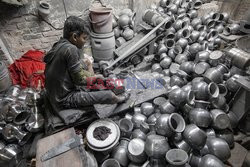 Workers use their feet to mould aluminium utensils in a factory