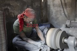Workers use their feet to mould aluminium utensils in a factory
